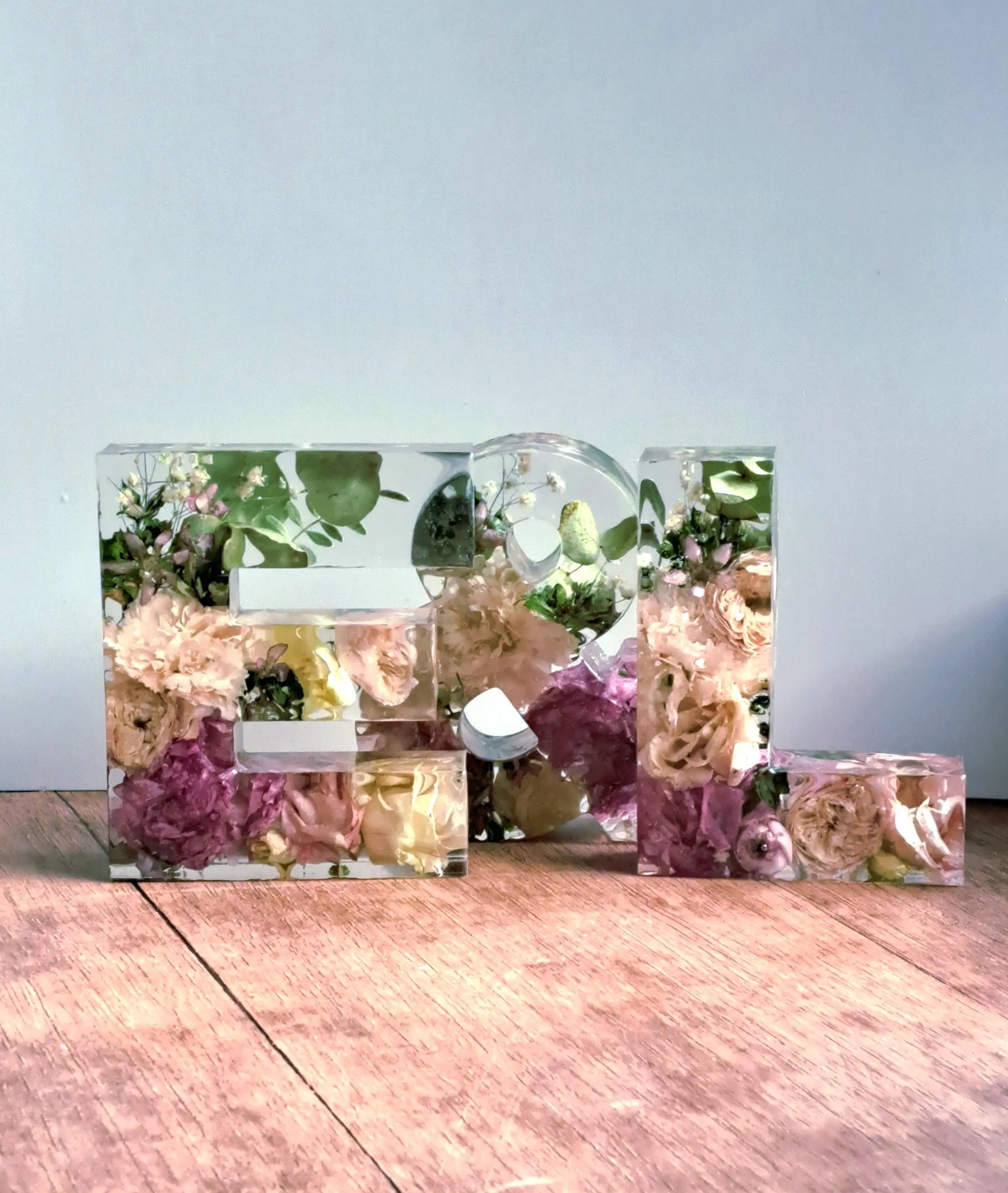 Die Schriftzug E & L aus klarem Epoxidharz mit eingearbeiteten, getrockneten Blumen aus dem eigenen Brautstrauß.