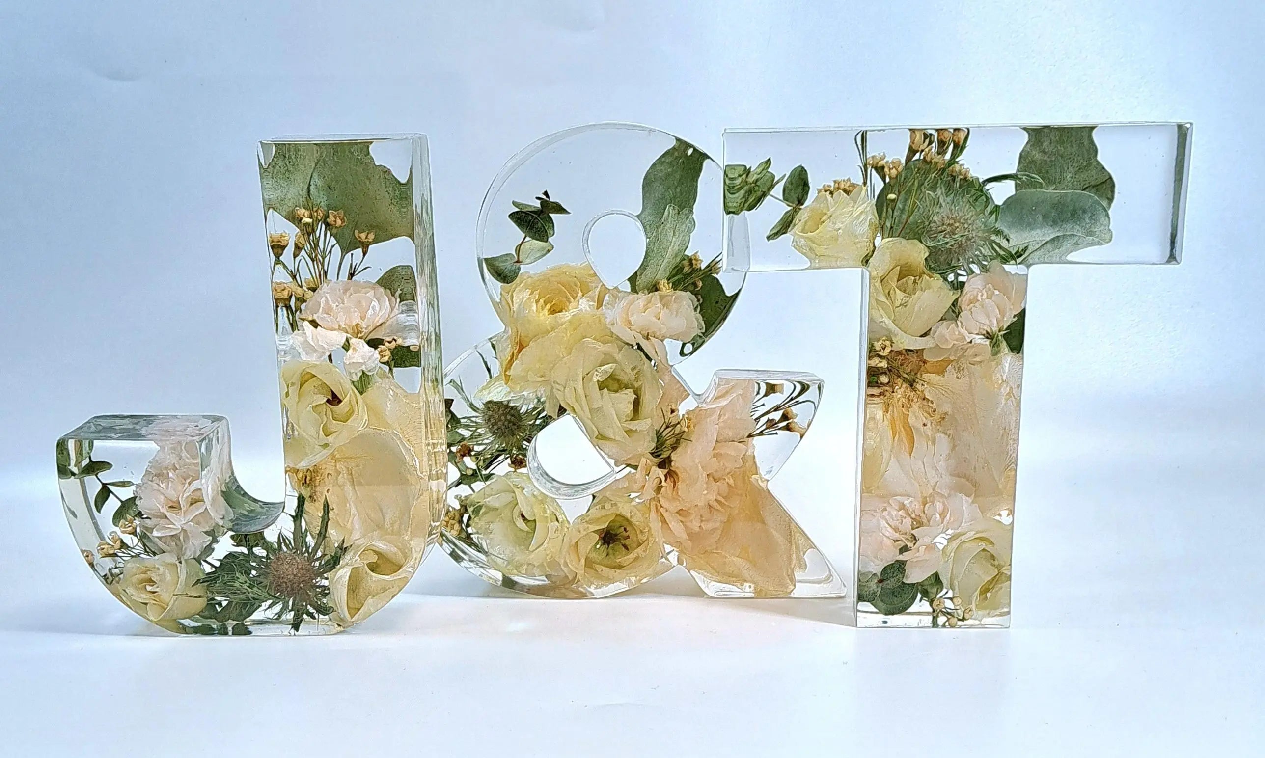 Schriftzug J & T aus Epoxidharz und vorwiegend weißen Blumen aus dem eigenen Brautstrauß. Wunderschön esthetisch arrangiert.